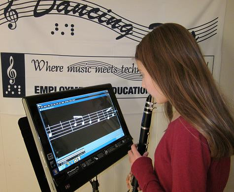 A person using a Lime Lighter device which is magnifying sheet music on a screen, to assist with reading it.
