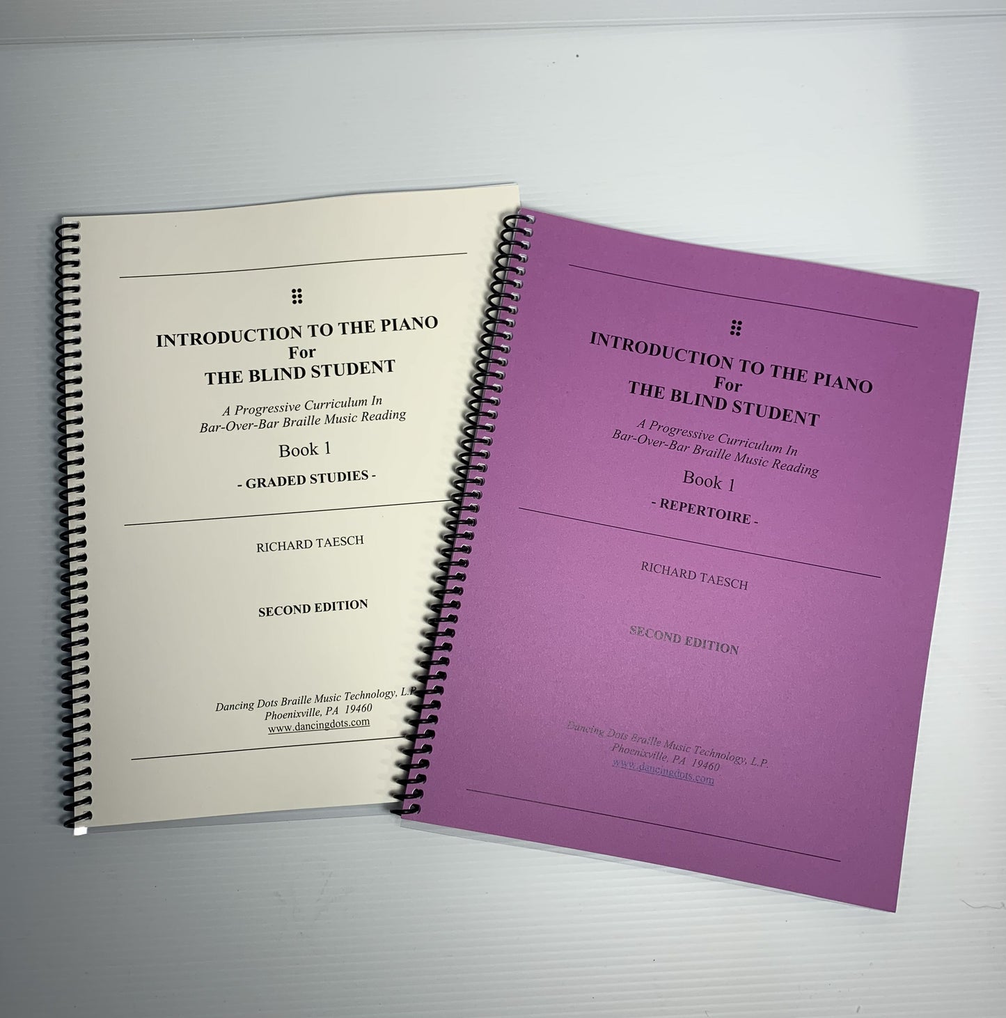 Two spiral-bound print books titled 'Introduction to the Piano for the Blind Student' on a light gray background.